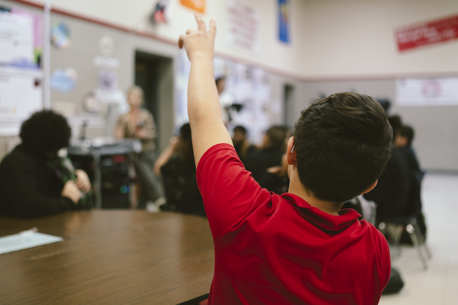 Child in red polo raising hand
